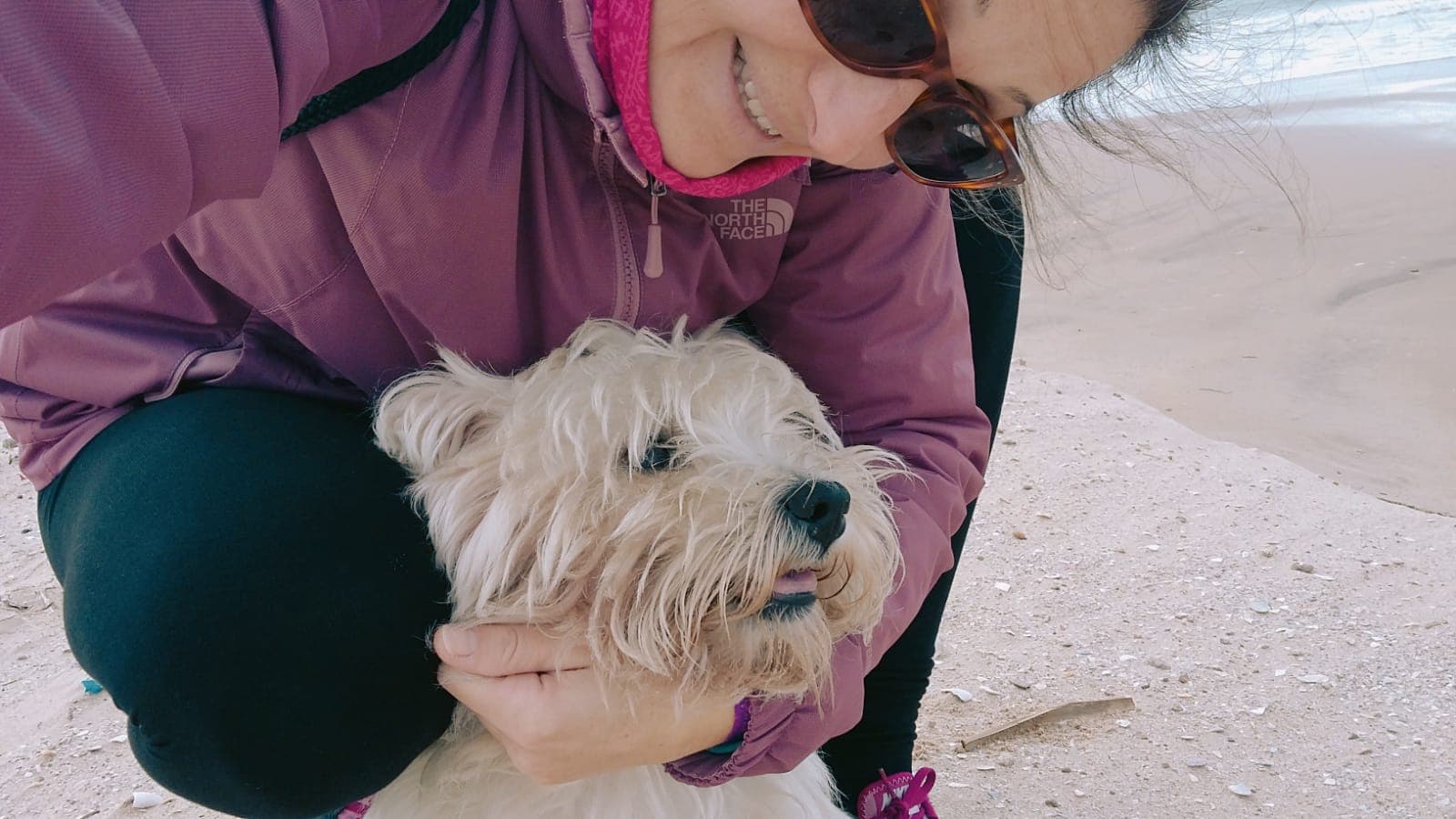 La cuidadora de Huellario abrazando con cariño a un perro pequeño en la playa